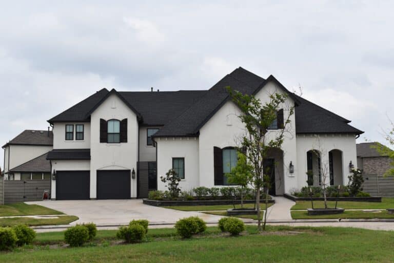 Large modern luxury home with white exterior, dark roof, manicured lawn, and landscaped front yard