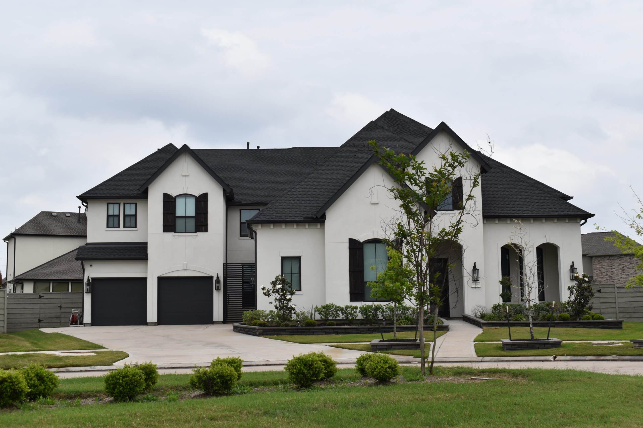Large modern luxury home with white exterior, dark roof, manicured lawn, and landscaped front yard